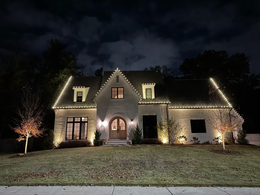 Residential home at night with classic warm white Christmas lights along rooflines and exterior accents.