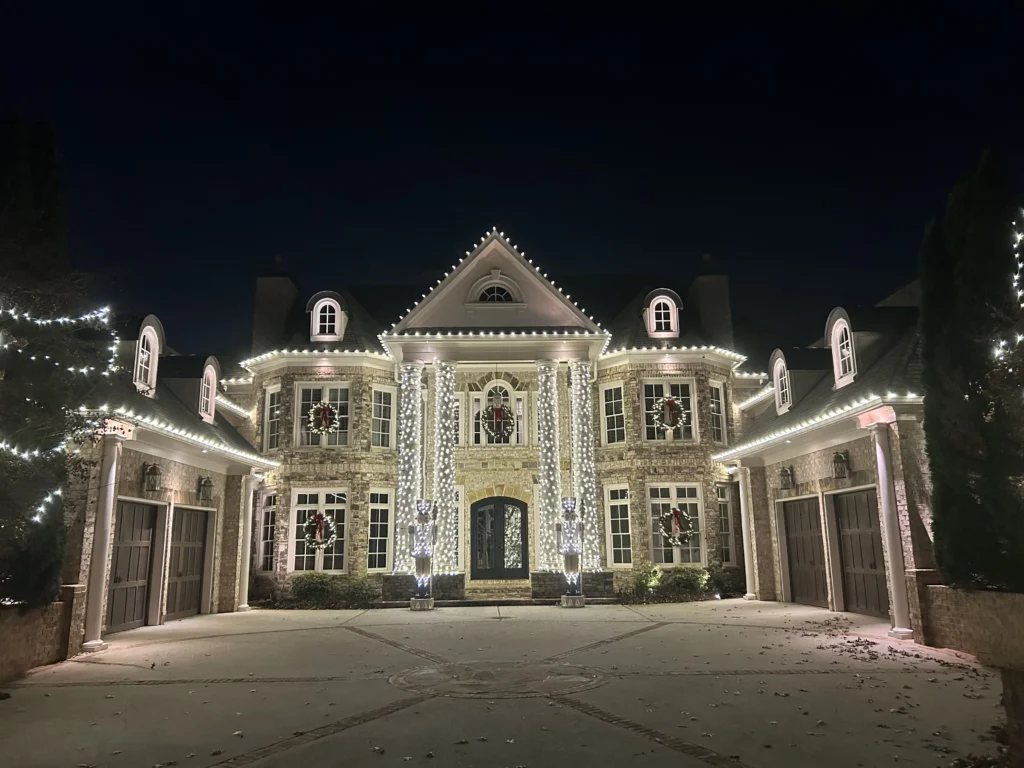 Large residential estate illuminated with warm white Christmas lights along rooflines and architectural details.
