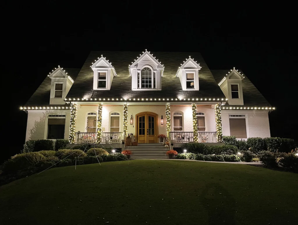 Luxury residential home illuminated with warm white holiday lighting across rooflines and entry features.
