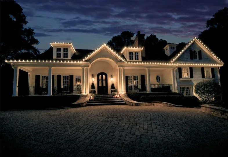 Large residential estate with warm white holiday lighting outlining rooflines and architectural details at dusk.