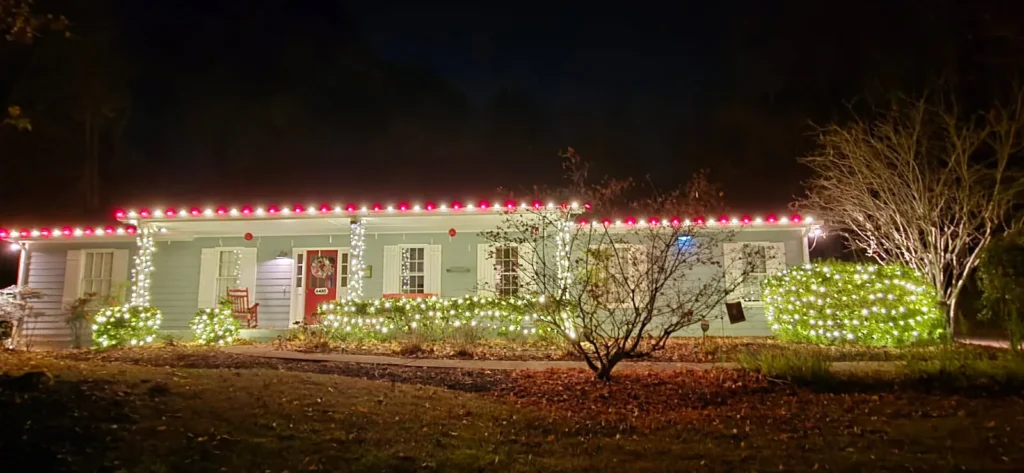 Single-story home decorated with red and white roofline Christmas lights and bright landscape accents.