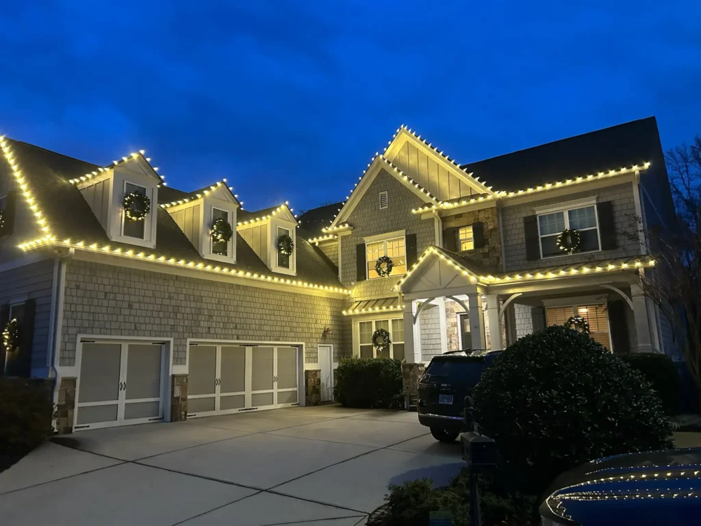 Two-story home with warm white lights tracing gables, rooflines, and front architectural features.